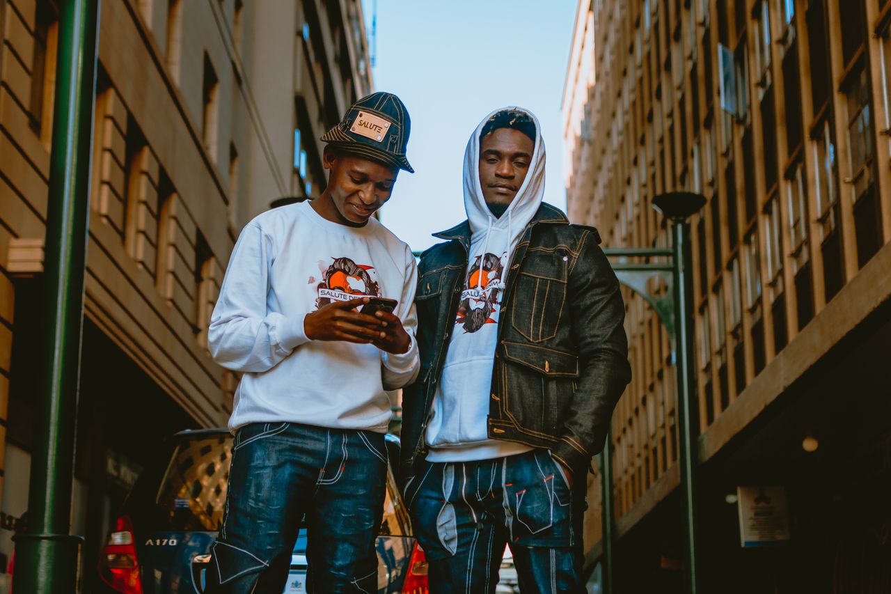 Contact Two young men in stylish urban fashion posing on a city street.