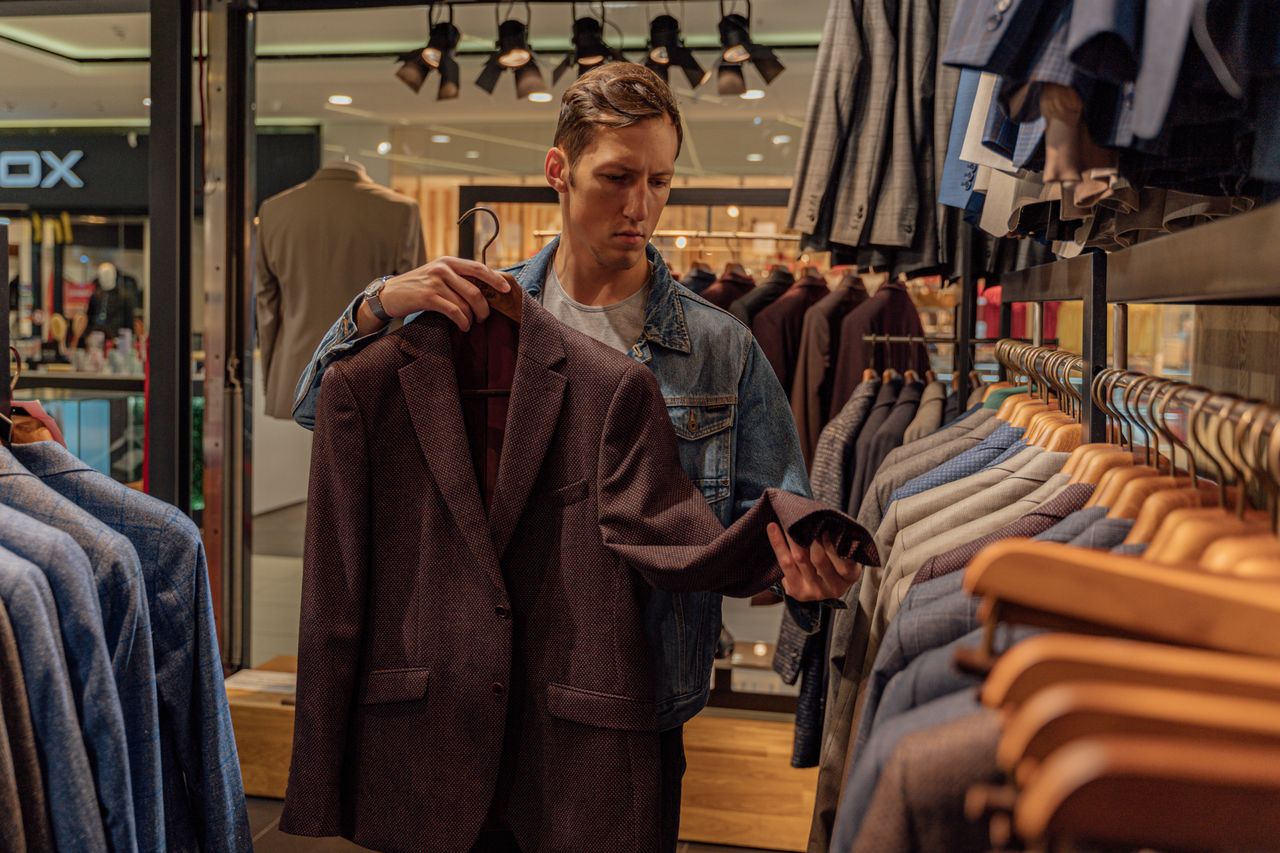 Services Man browsing stylish blazers in a modern clothing store, considering fashion options.