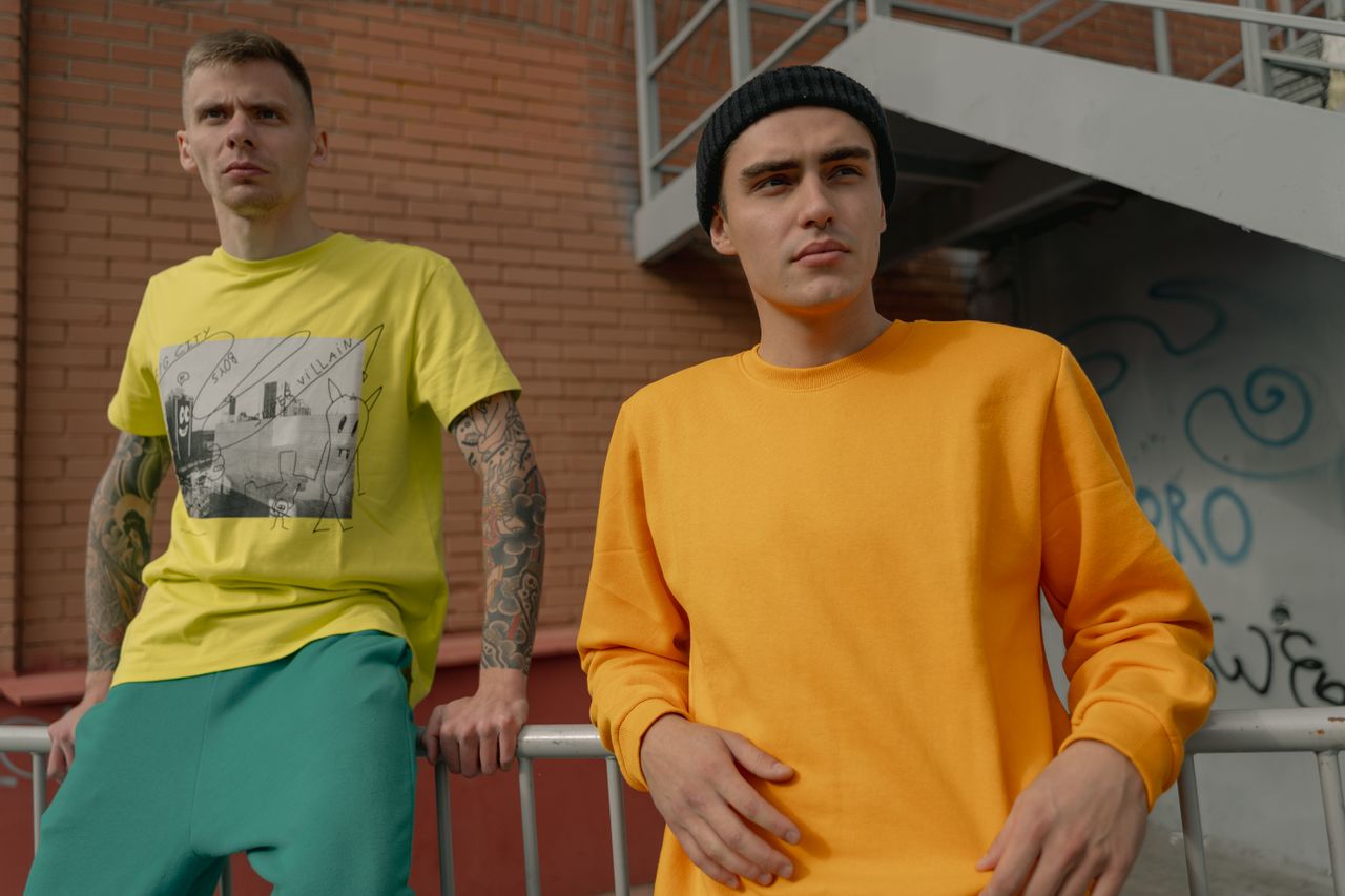 About Two stylish young men in casual streetwear pose against an urban backdrop.