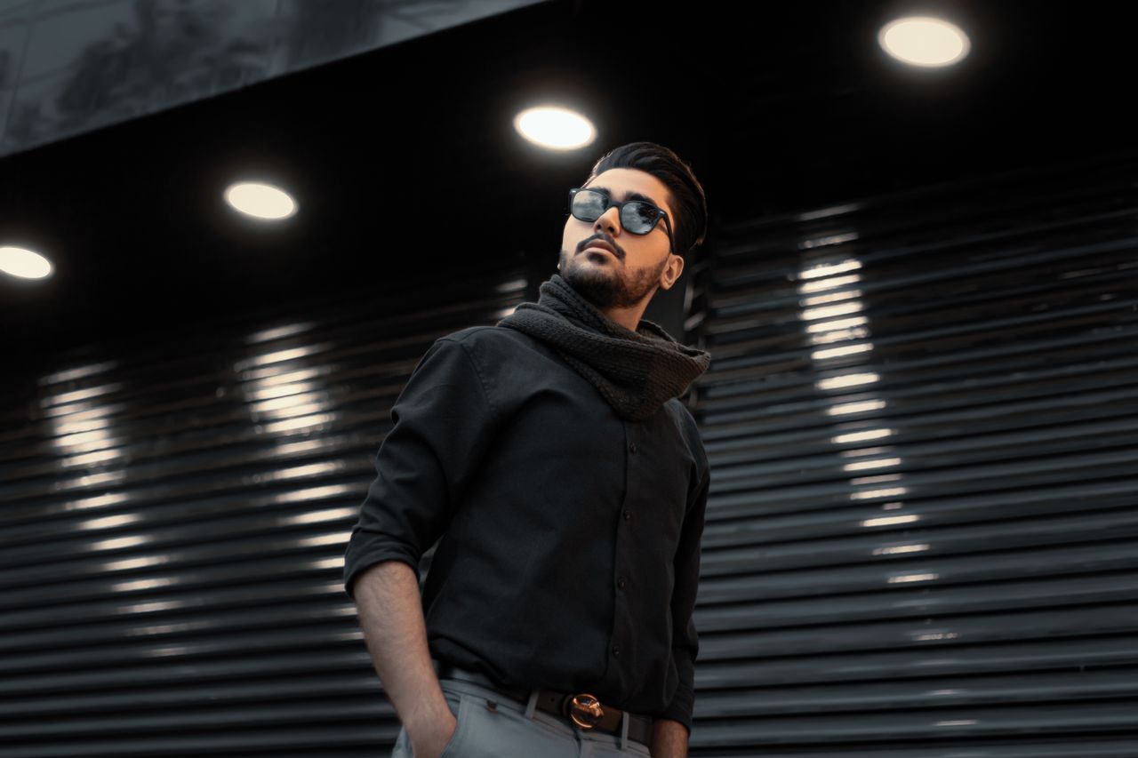 Services A fashionable man in sunglasses with a scarf poses under spotlights in an urban setting.